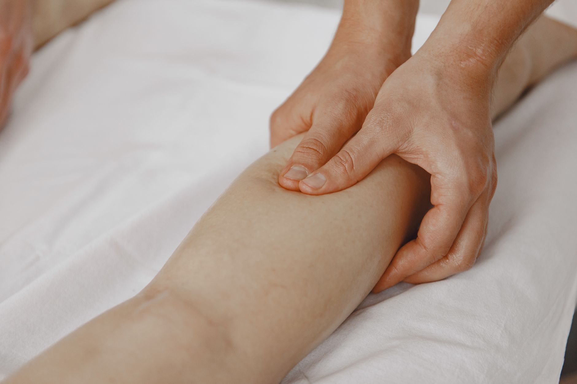 Close-up of a therapist's hands working the calf muscle of a client lying on white linens