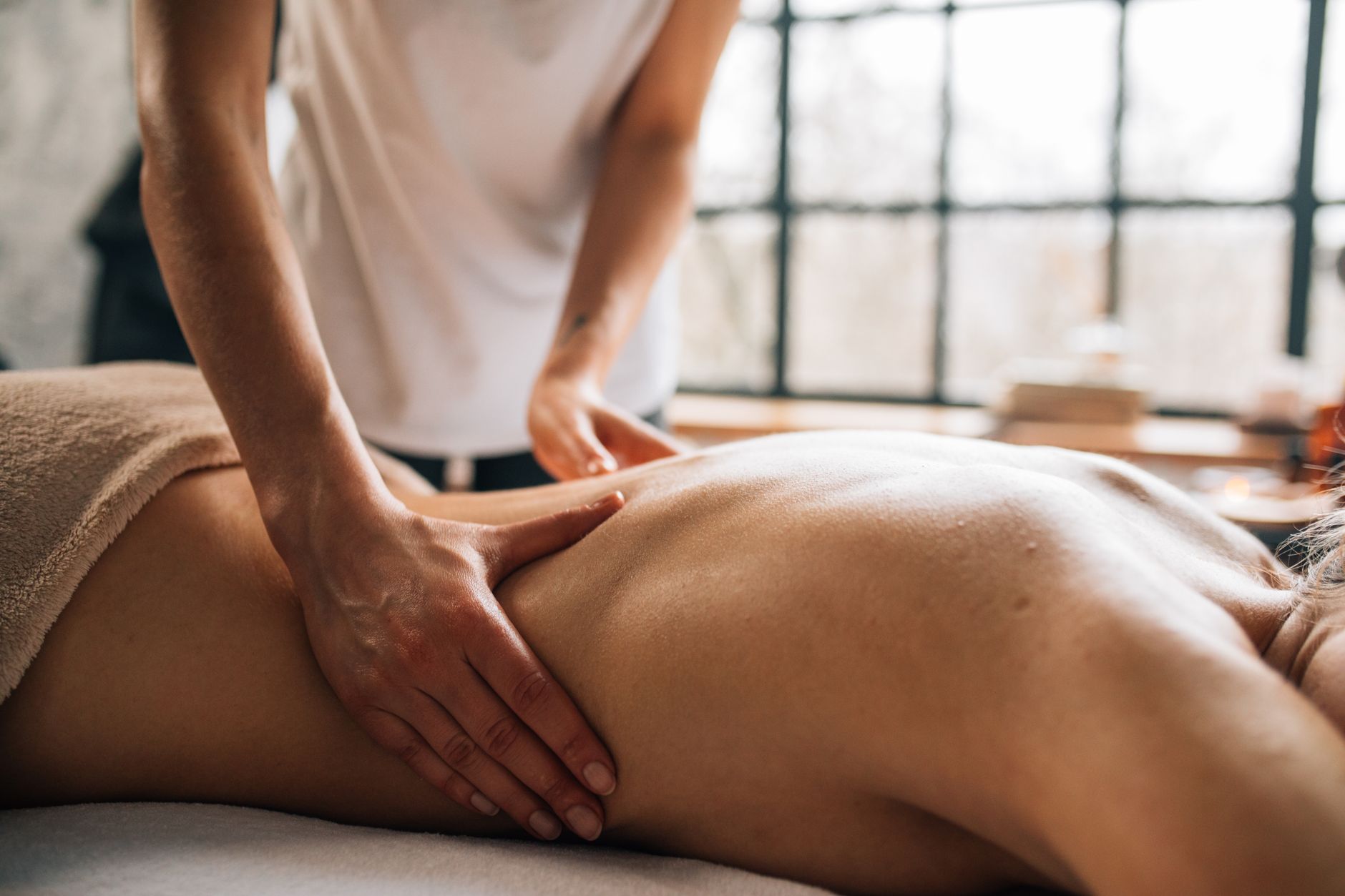 Massage therapist using long gliding strokes along a client's back in a sunlit treatment room